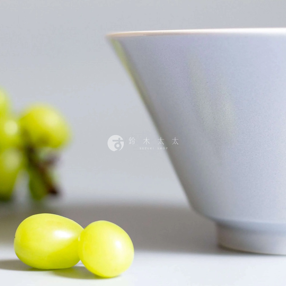Ciel 美濃燒簡約釉彩深碗，呈現柔和的淺灰色，碗口邊緣帶有細微的米色，碗身略帶顆粒感，材質為陶瓷。畫面左側有兩顆飽滿的綠色葡萄。