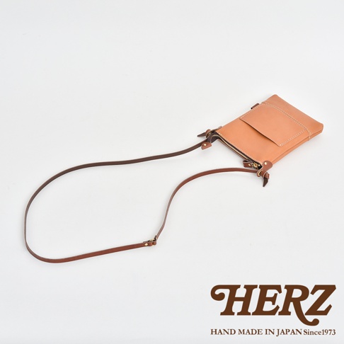 淺褐色皮革製作的直式隨身單肩包，包身設有拉鍊開合及外層翻蓋口袋，配有可調節的深棕色皮革背帶。