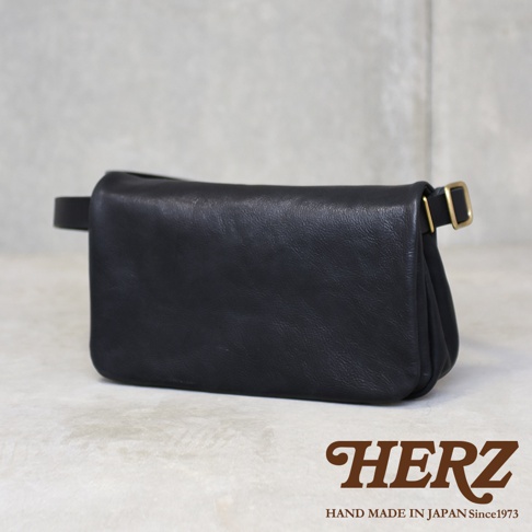 黑色皮革斜背包，款式簡約，配有可調節的金色搭扣。