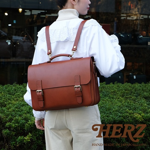 棕色皮革三用公事包，配有兩個前袋蓋和搭扣，頂部有提把，可轉換為背包模式。