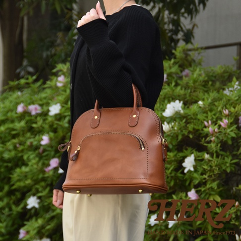 棕色皮革製成的經典貝殼手提包，配有頂部提把、正面拉鍊口袋和金色五金配件。