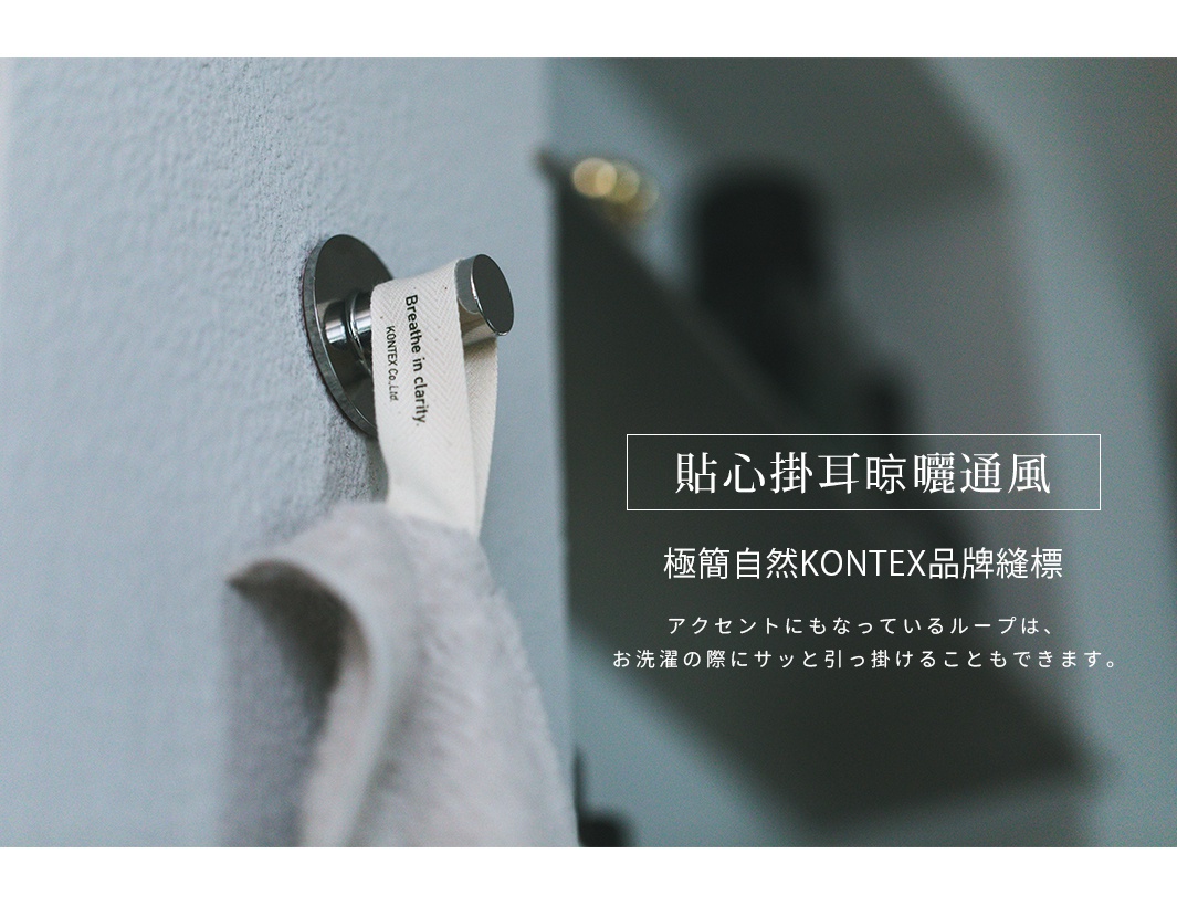 一張特寫照片，展示了掛在銀色金屬牆壁掛鉤上的KONTEX毛巾。毛巾上縫有一條印有Breathe in clarity與KONTEX品牌字樣的布標掛耳，方便懸掛晾曬與通風，體現簡約自然的居家設計風格。