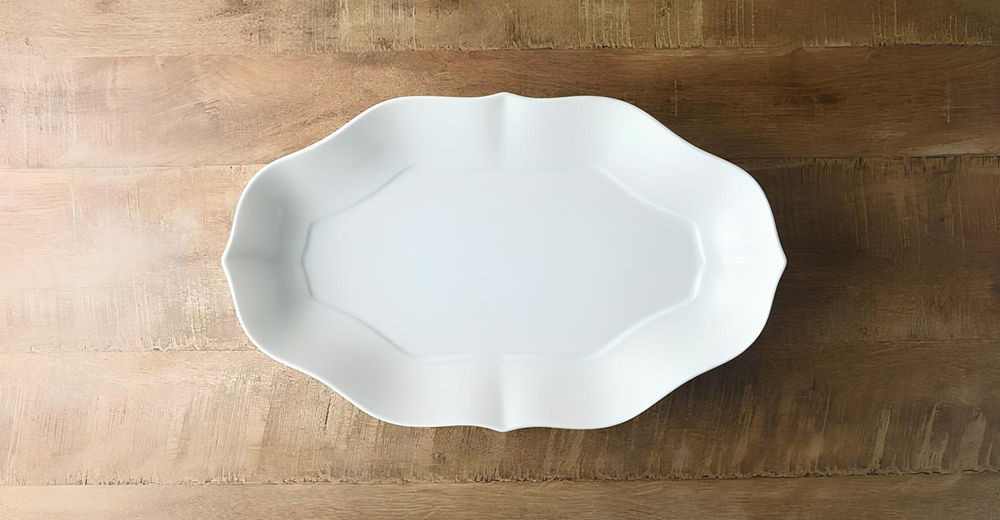 一個淡青白釉的美濃燒輪花長盤，呈現出輪廓分明的花瓣狀邊緣，盤身中央為八角形凹槽，置於木紋桌面上。