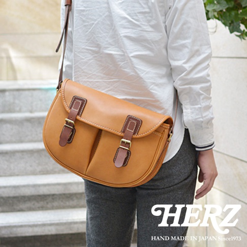 棕褐色皮革製成的傳統釣魚包，配有深棕色皮革裝飾和金屬扣。包款為斜肩包設計，設有雙扣蓋和可調節肩帶。