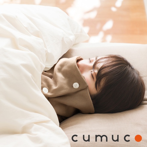 女性睡在床上，蓋著白色被子，頸部圍著卡其色頸套，上面有兩個鈕扣，下方有「cumuc」字樣和橘色圓點標誌。