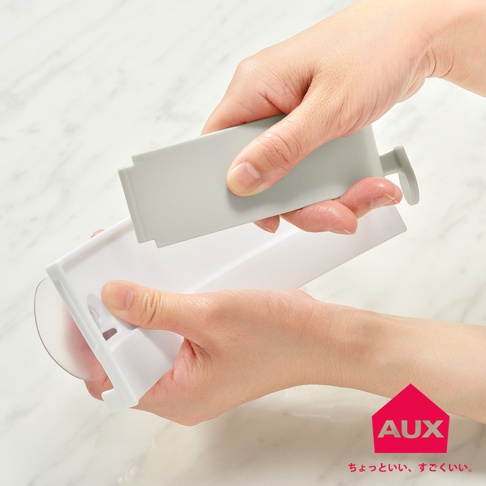 AUX 廚餘架，一只手將灰色蓋子裝入白色架子中。