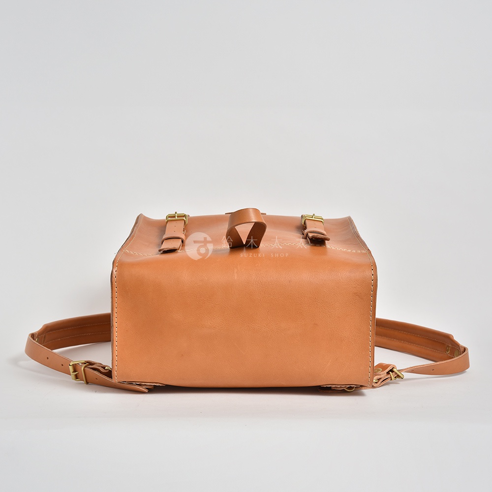 一款棕褐色皮革後背包，設計簡約，配有兩個可調節的搭扣帶和一個提把。包身結構方正，適合登山露營等戶外活動。