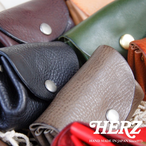 職人手作皮革零錢包，展示多種顏色，包括深棕、墨綠、黑色、灰褐色和橘色。皮革材質表面帶有自然紋理，每個零錢包都配有金屬按扣。