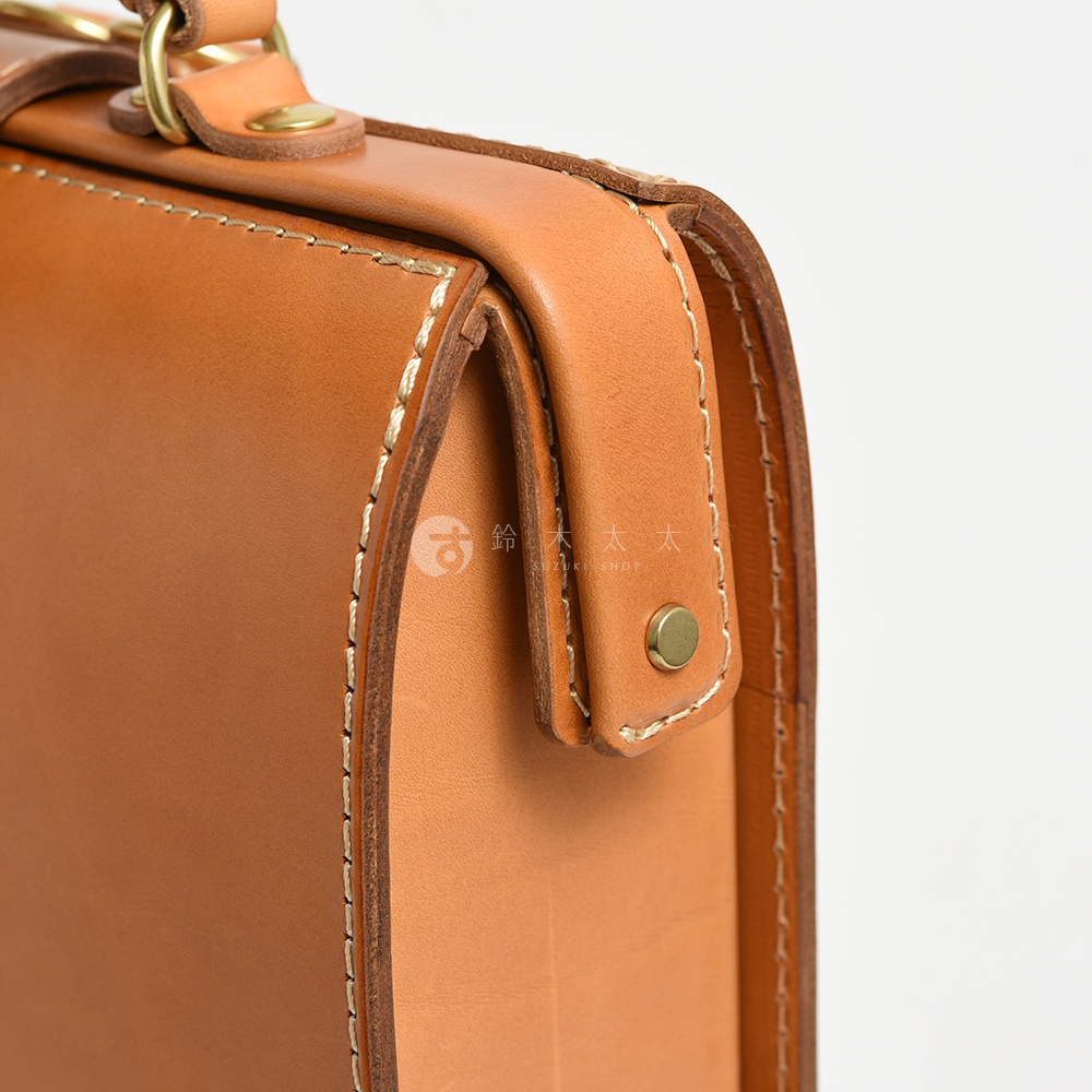 職人手作皮革杜勒斯商務後背包，採用鞣製皮革製成，呈現自然的棕褐色。包款細節包含車縫線、金屬铆釘與提把，展現紮實工藝。
