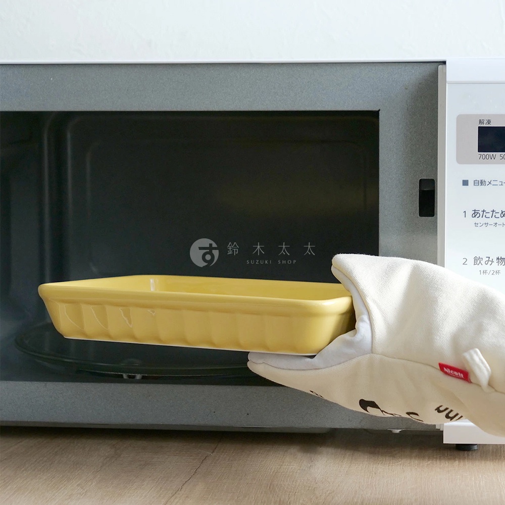 手持一個黃色美濃燒釉彩萬用長方烤盤，烤盤邊緣有條紋裝飾，正準備放入微波爐內。