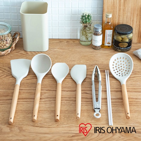 一套七件式廚房用具，包含白色矽膠鍋鏟、湯勺、漏勺、夾子和一雙筷子，皆配有木質手柄，擺放在木質檯面上。