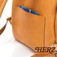 皮革休閒後背包，特寫其側邊的開放式口袋，內有藍色波點印花布料。整體為淺棕色皮革，搭配縫線細節與金屬扣環。