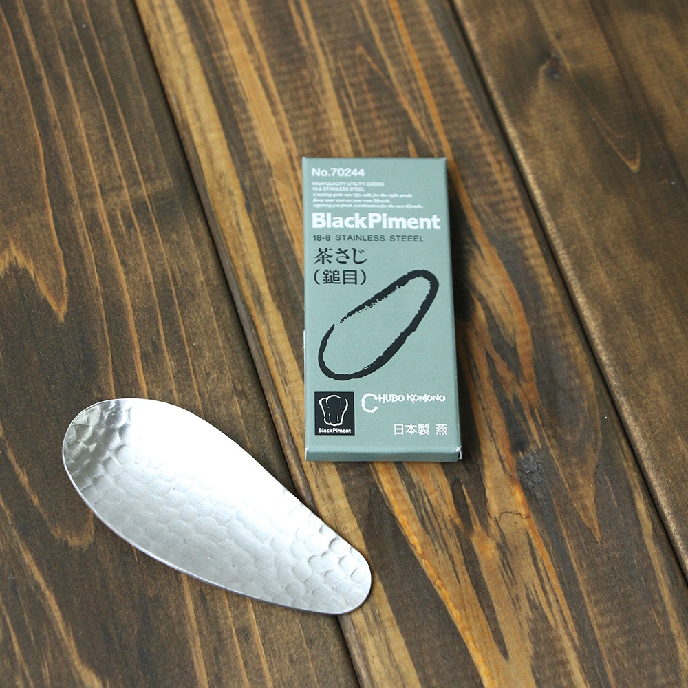 銀色不鏽鋼茶勺，表面有錘紋紋理，旁邊是印有「BlackPiment」及日文「茶さじ」字樣的淺綠色紙盒。