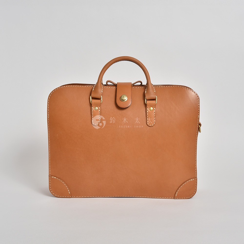 職人手作皮革三層收納兩用商務公事包，呈現焦糖棕色，採用天然皮革製成，結構紮實，設有提把及金屬釦環，設計簡約大方。