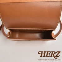 職人手作皮革翻蓋橫式單肩包，採用天然皮革製作，呈現溫潤的棕褐色。包款設計簡約，翻蓋處縫線清晰，內部空間一覽無遺，展現皮革的細緻質感。