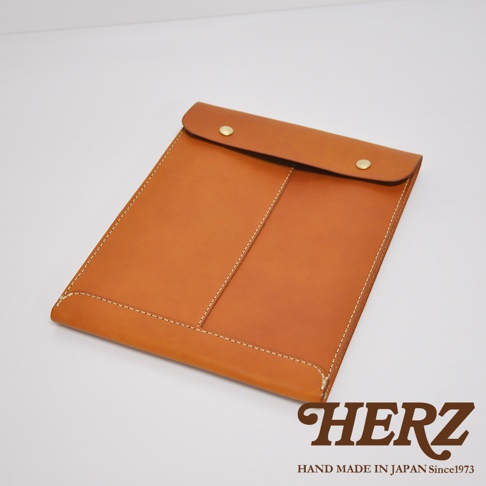 這是一款日本HERZ職人手作的皮革信封式手拿袋，採用淺棕色Latigo硬皮革製成，表面呈現簡潔的縫線細節與兩個金屬釦環，整體設計呈現平整的信封外觀，右下角印有HERZ品牌字樣。