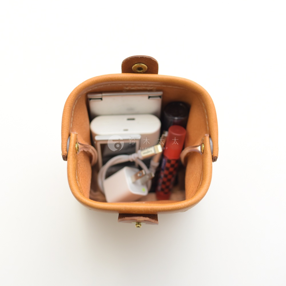 職人手作皮革口金化妝包 KF-143 S，淺棕色，開口設計，內部裝有充電器、充電線、耳機盒及口紅。
