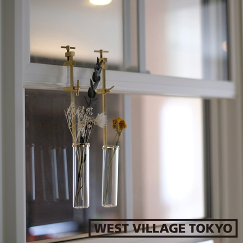 兩個黃銅可夾式玻璃花器，分別裝有白色乾燥花束和一朵黃色乾燥小花，懸掛在窗戶上。