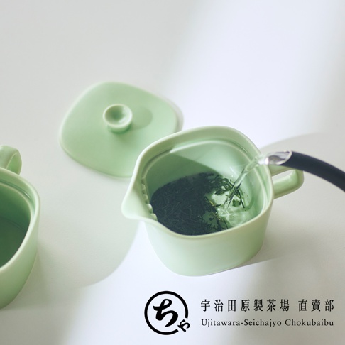 淡綠色美濃燒一人用茶壺，俯視視角拍攝正在注入熱水的過程，杯內裝有深綠色茶葉，旁邊放有壺蓋，右下方印有宇治田原製茶場直賣部的品牌標誌與文字。