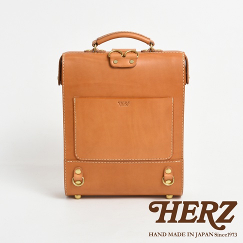 職人手作皮革杜勒斯商務後背包，淺棕色，經典方正造型，正面有品牌標誌壓印的方形置物袋，頂部有提把和金屬扣環，質感皮革與細緻車縫線。