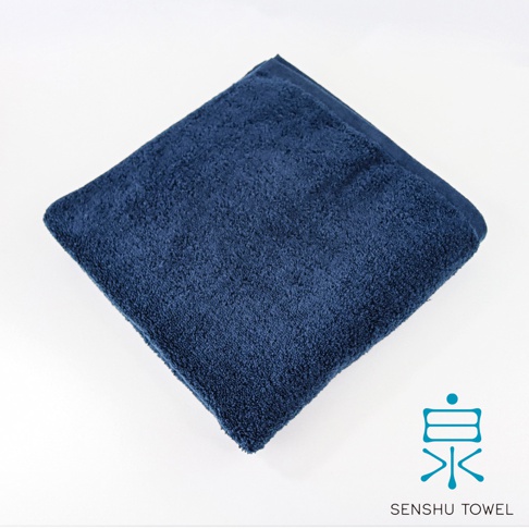 深藍色長纖浴巾，材質柔軟，質地蓬鬆，呈現高吸水性，角落帶有藍色「泉」字Logo及「SENSHU TOWEL」字樣。