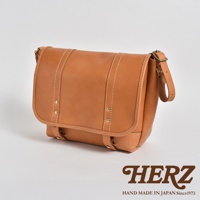 職人手作皮革復古郵差包，以天然棕色皮革製成，搭配白色車線及金色金屬扣飾，設計簡約實用。