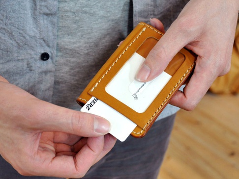 雙手操作的棕色皮革三面雙折票券收納夾，內有透明卡槽，可見卡片標誌「HERZ」和「Craftsmanship」。