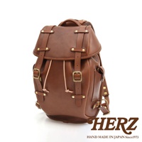 職人手作皮革經典雙扣後背包，呈現棕色澤，採用真皮材質，設有雙扣設計、抽繩束口及多個金屬扣環，風格復古。