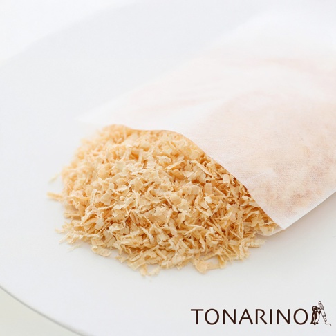 淺色無紡布包內裝有大量淡黃色、細碎的檜木屑，部分木屑散落在白色盤子上。