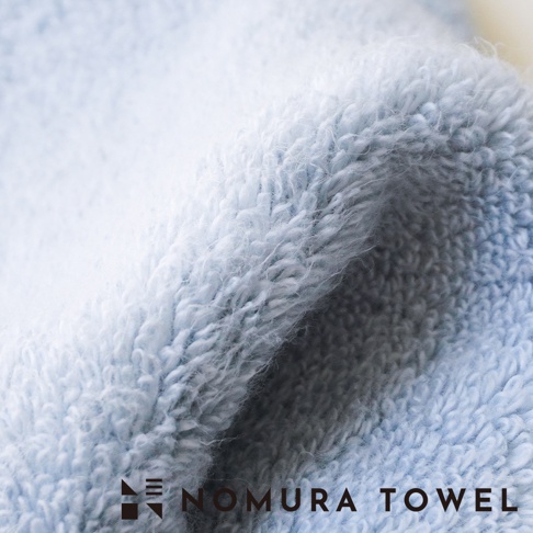 淺藍色毛巾材質的特寫，文字標示 NOMURA TOWEL