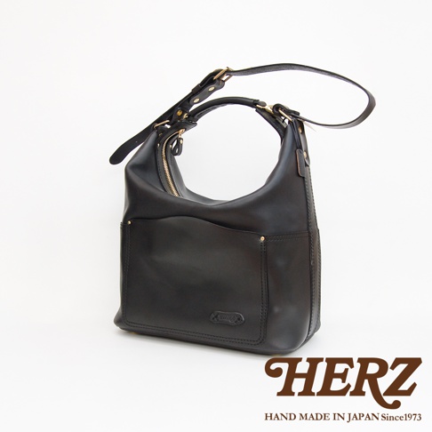 黑色厚實皮革製成的單肩波士頓包，包身有拉鍊開口，正面有兩個開放式口袋，口袋上方有品牌標誌，肩帶可調整，整體風格簡約。