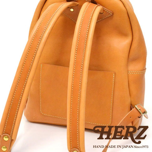 淺棕色皮革後背包，有兩條皮革肩帶，肩帶縫線清晰，包身背面有一個方形貼袋，整體風格休閒。