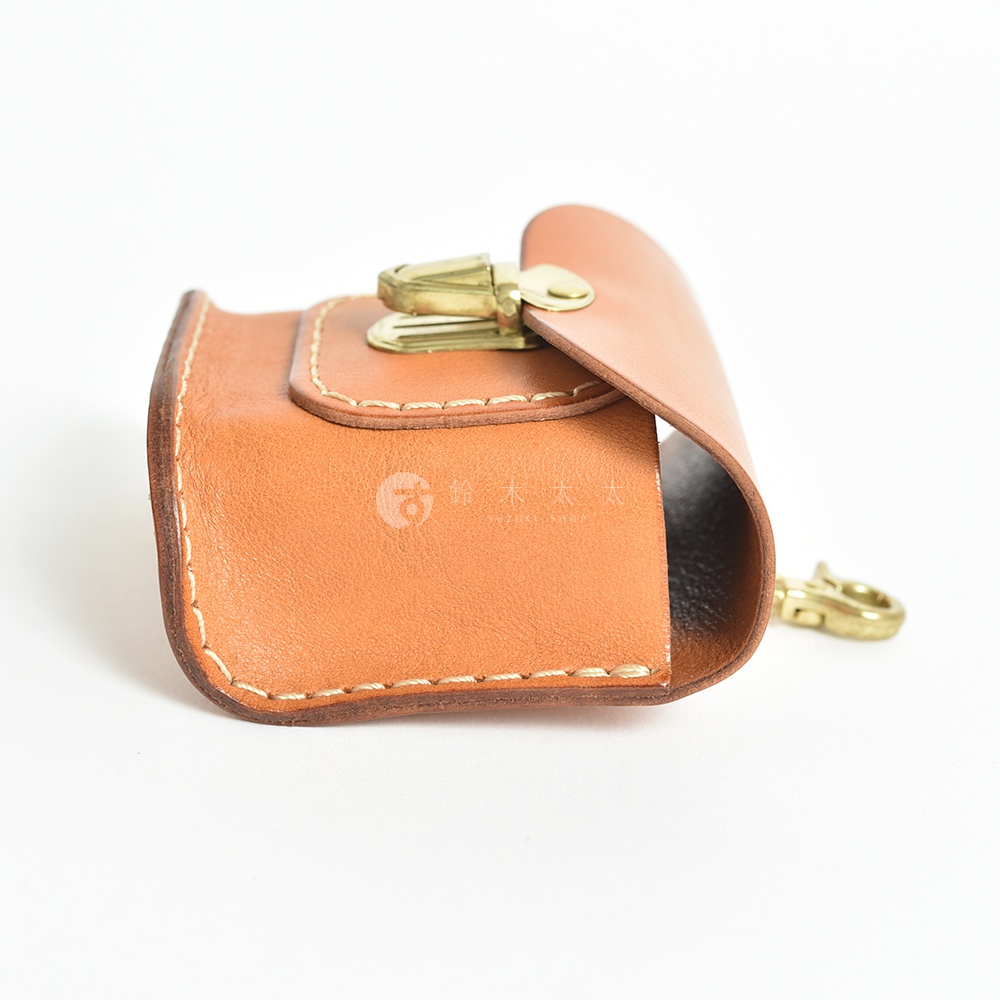 淺棕色職人手作皮革耳機收納包，採用真皮材質，搭配金色金屬開合扣和掛鉤，車縫線清晰。