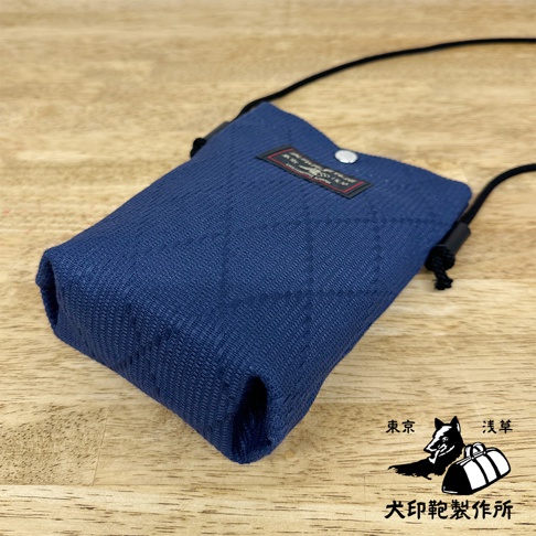 深藍色刺子織手機包，表面有菱格紋縫線，配有黑色細繩背帶及金屬按扣。