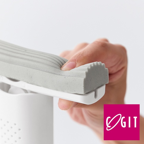 手持灰色條紋海綿刷，海綿柔軟且有彈性，刷頭邊緣帶有顆粒狀紋路，固定在白色刷柄上。