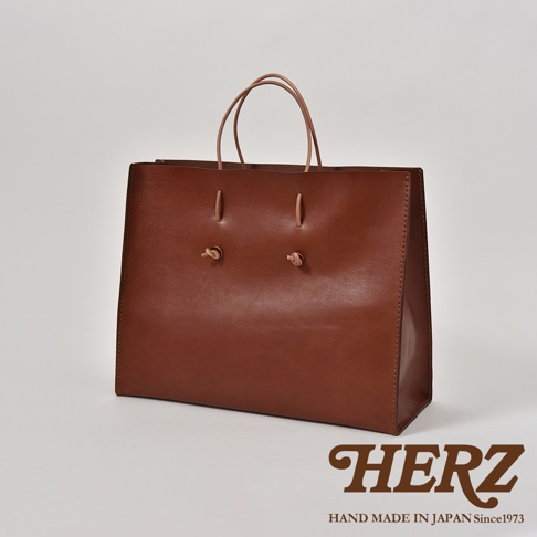 棕色皮革手提袋，簡約方形設計，配有兩條細皮革提把，正面中央有兩個皮革綁結裝飾。