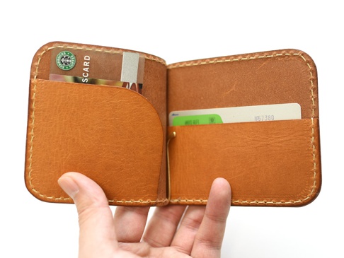 職人手作皮革橫式對折兩用收納短夾，呈現溫潤的淺棕色皮革，縫線清晰。內有卡槽，可放入多張卡片，設計簡潔實用。