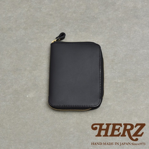 黑色皮革拉鍊式記事本收納包，附有金色拉鍊和皮革拉環，背景為灰色紋理表面。