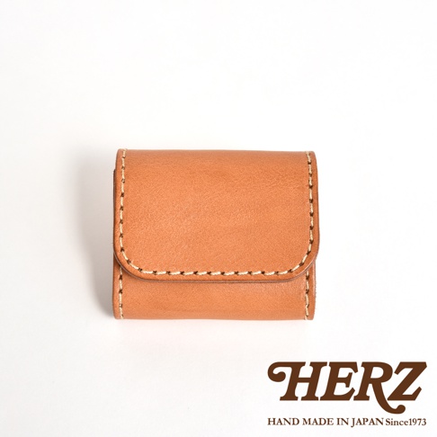 日本HERZ職人手作皮革零錢包，呈現簡約的棕色雙折式設計，採用優質Stare皮革製成，表面具有細膩的天然皮革紋理，邊緣以淺色縫線加固，右下角印有HERZ品牌標誌，整體風格精緻且具備日本手作工藝質感。