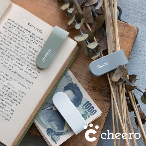 淺綠色、灰色和米白色萬能QQ變形夾，皆印有白色「cheero」字樣，其中淺綠色夾子夾在打開的書籍上，灰色夾子放在乾燥植物旁，米白色夾子則疊在日圓鈔票上。