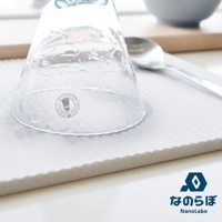 淺灰色波浪紋珪藻土置物墊，墊上有一只倒扣的透明玻璃杯，杯壁沾有水珠，旁邊放著一只銀色湯匙。