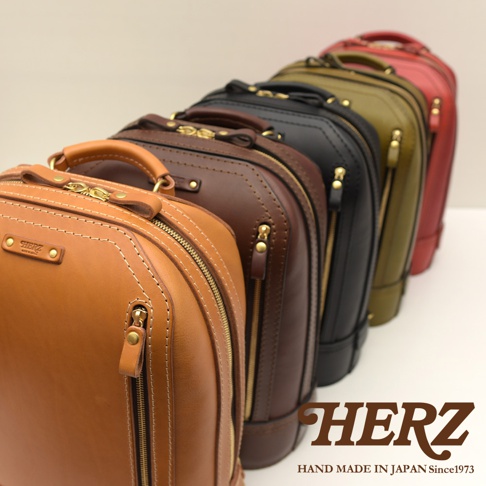 五個職人手作皮革立體商務後背包，依序為淺棕色、深棕色、黑色、軍綠色及紅色，皆配有金色拉鍊和提把。