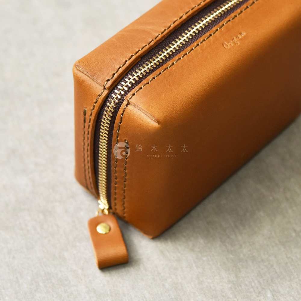 一個棕色皮革製成的箱型收納包，配有金色拉鍊和皮革拉把，包身上有壓印的品牌標誌。