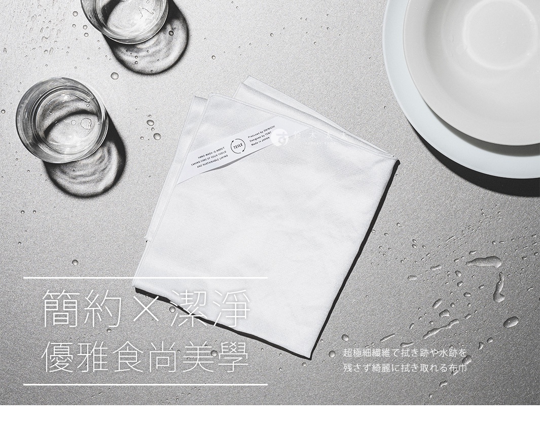 一疊純白色纖維擦拭巾，材質柔軟，表面帶有細微光澤，疊放在灰色紋理的桌面，旁邊有兩個玻璃杯和一個白色盤子，桌面散落著幾滴水珠。