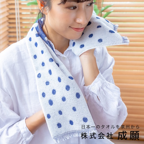 一位女性將藍白圓點圖案的嫘縈毛巾搭在肩上，毛巾觸感柔軟，邊緣有流蘇設計。