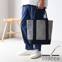 一款黑色與白色格紋刺子織托特包，配有黑色提把和底部，由三河木綿製成，由一人手持。