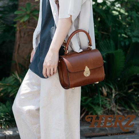 職人手作皮革復古杜勒斯手提包，以棕色皮革製成，配有金色鎖扣和腳釘，適合斜挎或手提。