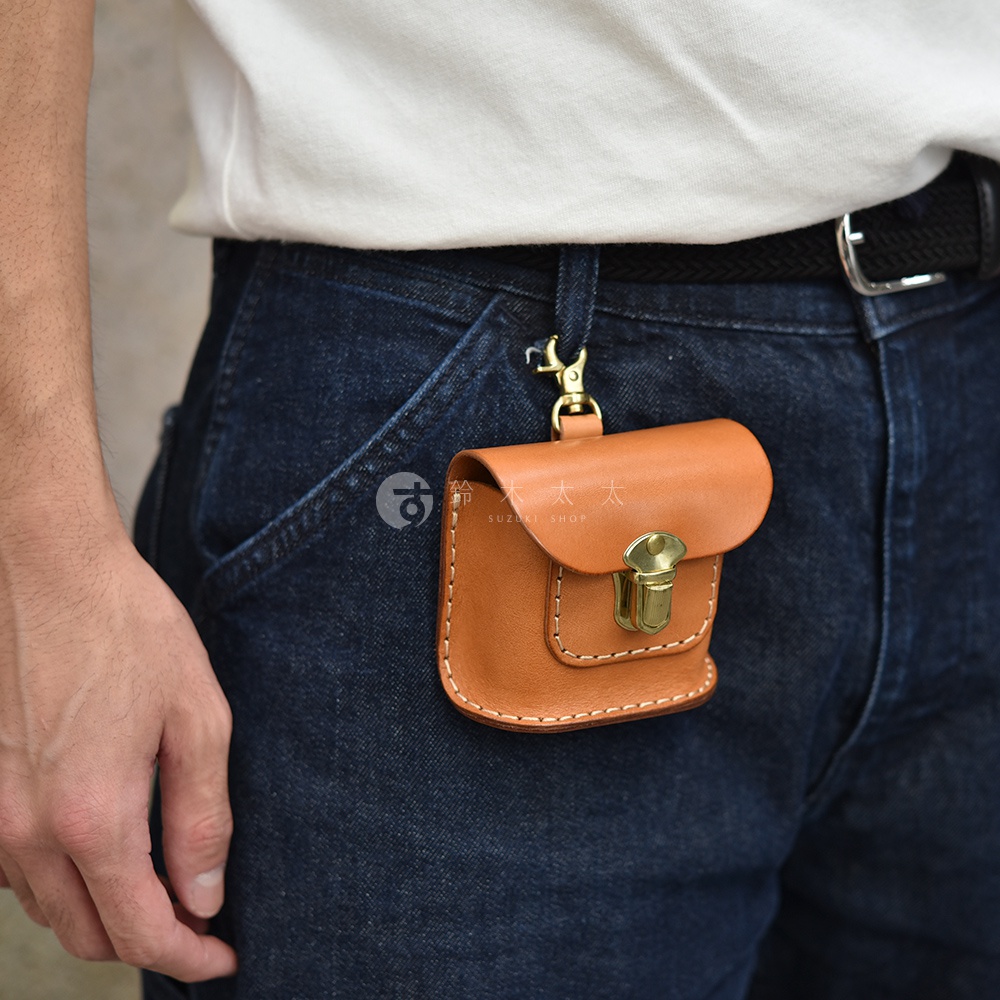 咖啡色皮革耳機收納包，附有金色金屬扣環和鉤子，可掛在牛仔褲腰帶上。