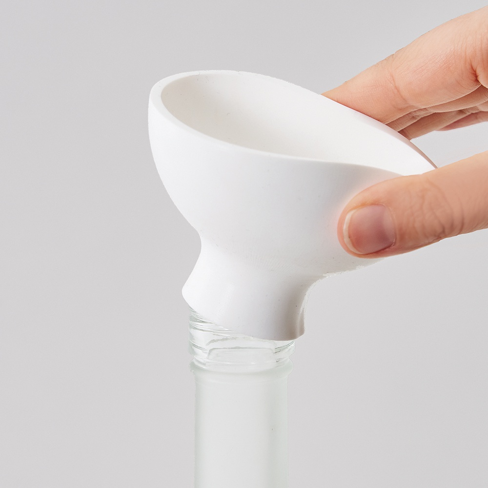 一個白色漏斗，由塑膠製成，其細長的漏斗頸插入一個透明玻璃瓶的瓶口。一只手握住漏斗的寬闊頂部。