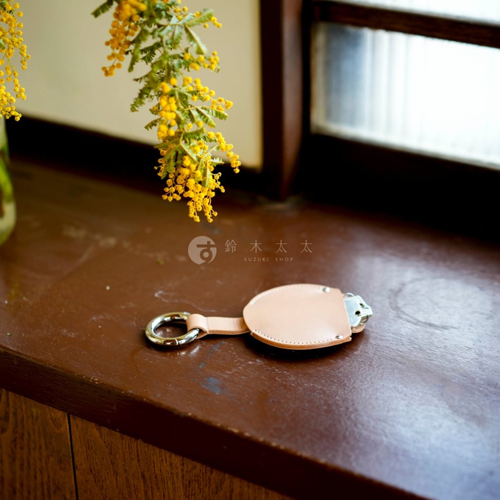 FABRIK 皮革圓型收納鑰匙圈，搭配銀色鑰匙環，懸掛於褐色木質檯面，背景為黃色枝葉與窗景